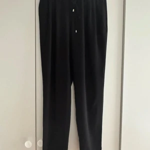 Svarta pull-on byxa med snörning - Svarta byxor med avslappnad passform och dragsko i midjan. Byxorna har raka ben, sidfickor och en bakficka med knapp. Perfekta för en chill och stilren look