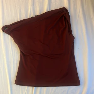 Vinröd oneshoulder topp Gina Tricot - Snygg vinröd topp från Gina Tricot i oneshoulder-modell. Toppens stilrena design och stretchiga material gör den perfekt för dig som vill sticka ut. Passformen är normal och tyget är mjukt och följsamt. Nypris 299 kr.