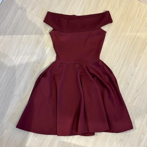 Vinröd offshoulder klänning Boohoo - Supersnygg vinröd kortklänning från Boohoo med offshoulder-modell och utsvängd kjol. Klänningen har en tight överdel och markerad midja. Materialet är mjukt och följsamt, vilket gör den bekväm att bära.