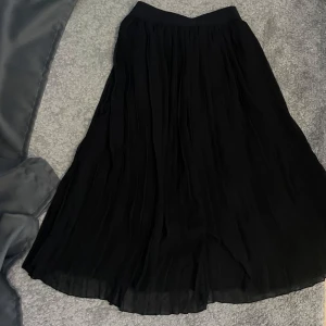 Svart plisserad långkjol från NA-KD - Svart plisserad långkjol från NA-KD i flowigt och lätt material. Kjolen har bred resår i midjan och är helsvart utan mönster. 