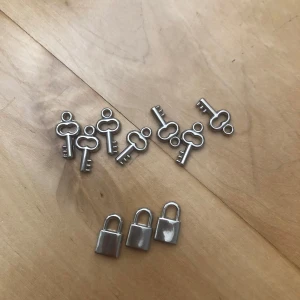 Silverfärgade berlocker lås & nycklar - Säljer ett set med 10 st små berlocker i form av silverfärgade hänglås och nycklar. Perfekta till att göra egna halsband, armband eller örhängen. Metallfinish med klassisk nyckel- och låsdesign, passar dig som gillar att pyssla med smycken och DIY-projekt. Det är 3 st lås och 7 st nycklar i detta pack. 