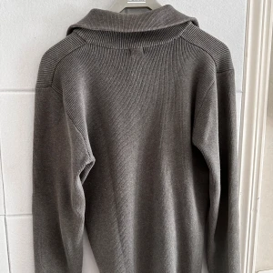 Grå half zip tröja från Filippa K - Säljer en stilren grå ribbstickad tröja från Filippa K med half zip och krage. Tröjan är i 100% bomull och har långa ärmar. Perfekt för dig som gillar en clean och avslappnad look.