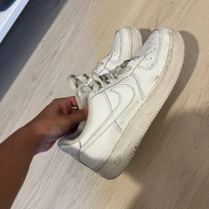 Vita Nike Air Force 1 sneakers - Klassiska vita Nike Air Force 1 sneakers med låg profil och rund tå. Skorna har snörning och är tillverkade i skinn med en platt sula. Perfekta för en clean och stilren look. 