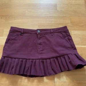 Jeanskjol volang - Säljer denna vinröda lågmidjade volang jeanskjol. Saknar storlekslapp men skulle uppskatta att den är ca M/38. Obs, volangerna är påsydda i efterhand, alltså ej på kjolen originellt. 