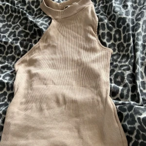 Beige ribbad ärmlös polotopp - Snygg beige polotopp med ribbad struktur och ärmlös design. Toppen har hög hals och är perfekt för att styla med jeans eller kjol. Enkel men trendig look som passar till många outfits.