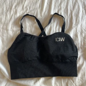 Mörkgrå linnetopp från ICANIWILL - Mörkgrå linnetopp från ICANIWILL med smala korsade axelband och halvt öppen rygg. Toppen har en ribbad nederkant och diskret logga framtill. Perfekt för träning och har en tight passform som sitter på plats under alla rörelser.🩶