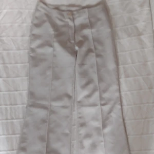 Skitsnygga utsvängda Y2K beige byxor/kostymbyxor - Skitfina beige kostymbyxor med vida ben och sydda pressveck både i fram och i bak, vilket gör att de är väldigt snygga på. Byxorna har medelhög midja och stängs med knapp och dragkedja. Perfekta för en clean och stilren look. Finns en del småfläckar längst ner i bak. Storlek XS/S.