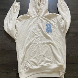 Vit hoodie med blå Risky märke  - Säljer en oversized vit hoodie med stor blå Risky märke  på bröstet och coolt Risky -tryck på huvan. Klassisk känguruficka framtill och mjukt material, perfekt för chill dagar. Långärmad och med huva för extra cozy vibes.