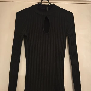 Svart ribbad långärmad tröja - svart ribbad tröja med lång ärm och en cool keyhole-detalj vid halsen. Tröjan har en tight passform och är perfekt för dig som gillar stilrena plagg med en twist. 