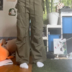 Olivgröna cargopants med vida ben - Säljer ett par olivgröna cargopants med bred passform och vida ben. Byxorna har flera fickor på sidorna och knytband i midjan för extra cool look. Perfekta för dig som gillar streetstyle och avslappnad vibe.