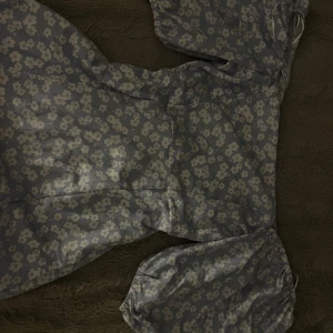 Blommig blå långklänning med puffärm - Supersöt långklänning i ljusblått med vita blommor och puffiga kortärmar. Klänningen har en smickrande passform och en liten slits framtill. Perfekt för sommarens alla tillfällen och ger en romantisk vibe.