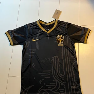 Svart Brasilien fotbollströja Nike - Snygg svart kaktus Brasilien fotbollströja från Nike med guldiga detaljer och broderat CBF-märke på bröstet. Jag säljer den för att den inte passar mig. Storlek S. Skriv i dm om du har frågor. 