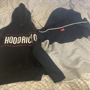 Nike och Hoodrich hoodies XL - Två hoodies i storlek XL. En svart Hoodrich med vit logga och röda detaljer samt snörning i huvan. En Nike hoodie i mörkblått och grått med vit Nike-logga och vit rand över bröstet. Båda har huva och långa ärmar, perfekta för chill eller streetwear. Hoodrichen har ett litet hål i armen men man märker inte Nike tecken är 1 månad gammal 