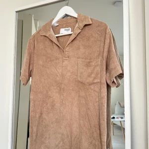 Beige frotté piké från Selected Homme - Säljer en beige kortärmad piké från Selected Homme i mjuk frotté. Piken har en öppen krage, bröstficka och avslappnad passform. Perfekt för dig som gillar en chill och trendig stil.