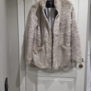 Beige pälsjacka från ONLY - Snygg beige pälsjacka från ONLY med långärmad design och två fickor framtill. Jackan har en mjuk och fluffig känsla, perfekt för att hålla värmen under kyliga dagar. Enkel att matcha med olika outfits och ger en lyxig vibe.
