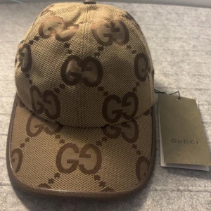 Beige Gucci keps - Skicka dm för video. Storlek ”M” Snygg keps från Gucci i beige och brunt med det klassiska GG-monogrammet över hela kepsen. Kepsen har böjd skärm, justerbar rem bak och är tillverkad i slitstark canvas. Perfekt för dig som vill sticka ut med en lyxig accessoar.