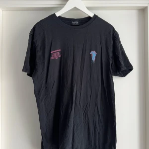 Limited edition Quavo top - Cool svart t-shirt från BoohooMAN x Quavo collab med färgstarkt grafiskt tryck i blått och rosa på ryggen och mindre tryck framtill. Skön passform och tillverkad i 100% bomull. Perfekt för dig som gillar streetstyle och unika prints.