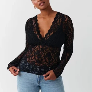 Svart spetsblus från Gina tricot - Supersnygg svart blus i spets från Gina tricot med djup v-ringning och långa ärmar. Blusen är genombruten med blommigt spetsmönster och har en feminin, figurnära passform. Perfekt att styla med jeans eller kjol för en trendig look.