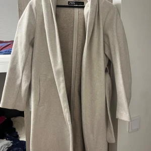 Beige kappa med bälte från Zara XS - Snygg beige kappa från Zara i storlek XS. Modellen har en avslappnad passform, knyts med bälte i midjan och har stora slag. Perfekt för dig som gillar stilrena och enkla plagg med lite extra edge.