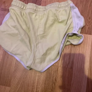 Ljusgula sportiga shorts med vit kant - Snygga ljusgula shorts med vit kant och elastisk midja. Modellen är sportig med rundade ben och fickor på sidorna. Perfekta för varma dagar eller när du vill ha en chill och bekväm stil.