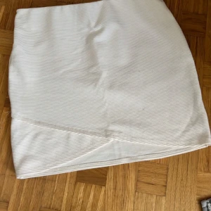 Vit ribbad kortkjol från Cubus - Säljer en vit ribbad kortkjol från Cubus med diskreta horisontella ränder. Kjolen har en enkel och clean look med lätt omlott-effekt framtill. Perfekt för dig som gillar minimalistisk stil och vill ha något som är lätt att matcha.