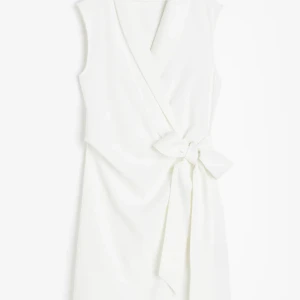 Vit omlottklänning med knyt - Snygg ärmlös vit omlottklänning med knyt i midjan och v-ringad hals. Klänningen har en elegant och enkel design som ger en fräsch look. Perfekt för dig som gillar stilrena plagg med fina detaljer.