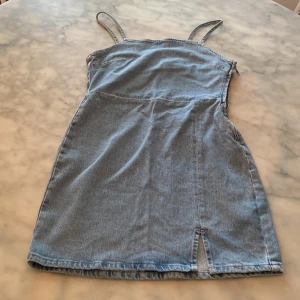 Blå jeansklänning med dragkedja - Jättefin kort jeansklänning ifrån Bik Bok i ljusblå denim med smala axelband och en liten slits framtill. Klänningen har figurnära passform och dragkedja i sidan. 💕