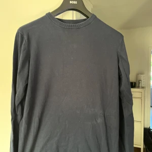 Mörkblå långärmad tröja Indicode - Säljer en stilren mörkblå långärmad tröja från Indicode. Tröjan har rund halsringning med ribbad kant och är tillverkad i en mjuk bomullsblandning. Perfekt för dig som gillar enkel och clean stil.