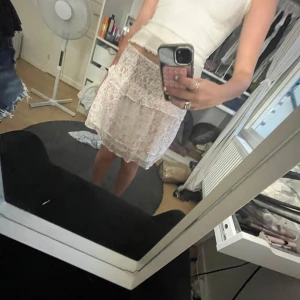 Söt blommig volangkjol i ljusa toner - Supersöt kort kjol med blommigt mönster i ljusrosa och vitt. Kjolen har volangdetaljer och en romantisk vibe, perfekt för varma dagar. Sitter normalt i midjan och är lätt att matcha med en enkel topp.