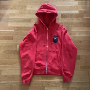 Röd Stüssy hoodie med 8-ball print - Röd hoodie från Stüssy med stor 8-ball print och logga på ryggen samt mindre print på bröstet. Tröjan är i bra skick.