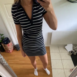 Marinblå randig kortklänning - Snygg marinblå kortklänning med vita ränder och v-ringning. Klänningen har krage och korta ärmar, sitter tight och har en sportig, fräsch vibe. Perfekt för dig som gillar en enkel men stilren look. strl M men funkar som S