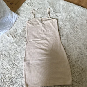 Beige ribbad kortklänning från Amisu - Säljer en beige ribbad kortklänning från Amisu med smala axelband och figurnära passform. Klänningen har en enkel och stilren design med tunna ränder i materialet, perfekt för en clean och trendig look.