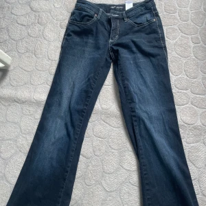 Mörkblå low bootcut jeans Arizona - Snygga mörkblå bootcut jeans från Arizona med coola broderade örnar och siffran 1973 på bakfickorna. Jeansen har kontrastsömmar och klassisk femficksdesign. Perfekta för dig som gillar en retro vibe och vill sticka ut lite extra. Priset går och diskutera !