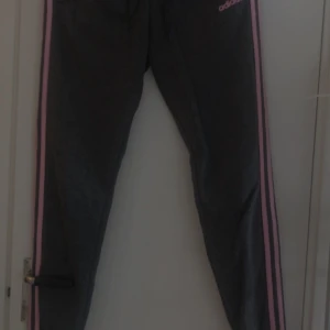 Adidas träningsbyxor med ränder - Två par Adidas träningsbyxor, ett par mörkgrå med rosa ränder och ett par svarta med vita ränder längs sidorna.  150kr /st