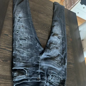 Svarta slim jeans Slim/Glenn 31/32 - Säljer ett par svarta slim fit jeans från Jack and Jones i storlek 31/32. Jeansen har slitna detaljer och en tvättad . Klassisk femficksmodell med knappar. Perfekta för dig som gillar en smal passform och streetstil.