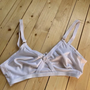 Vit bandeau-linnetopp med rosett - Supersöt vit bandeau-linnetopp med smala axelband och liten rosett framtill. Topp i mjukt, glansigt material som känns skönt mot huden. Perfekt att styla under skjorta eller som den är för en clean look.