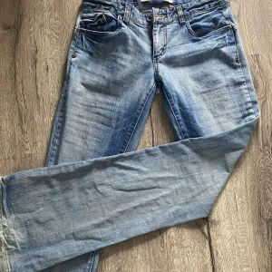 Blå jeans från Only Jeans, rak modell - Säljer ett par klassiska blå lågmidjade jeans från Only Jeans i utsvängd modell. Jeansen har fem fickor, slitna benslut och snygga slitningar längs benen. De är tillverkade i bomull och har orange kontrastsömmar. Perfekta för en avslappnad och cool stil.