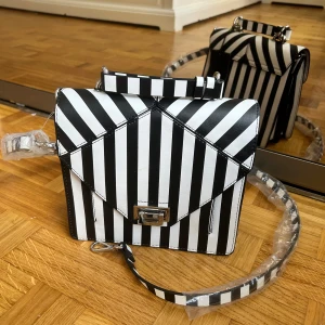 Randig svartvit axelväska från Zara - Säljer en riktigt snygg axelväska från Zara med svartvita ränder och cool geometrisk design. Väskan har både handtag och justerbar axelrem, samt flera fack inuti för att hålla ordning på dina grejer. Stängs med ett silvrigt spänne framtill.