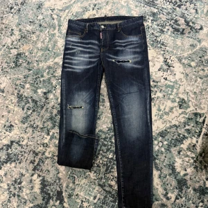 Dsquared2 slim jeans med broderi - Mörkblå slim fit jeans från Dsquared2 med slitningar och broderade blommor på bakfickan. Jeansen har klassisk femficksdesign, snygga slitdetaljer framtill och kontrastsömmar. Tillverkade i bomull med en cool, tvättad look. Priset är ej hugget i sten‼️