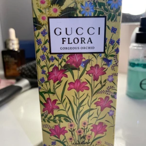 Gucci Flora Gorgeous Orchid Parfym - Gucci Flora Gorgeous Orchid är en lyxig parfym med en blommig doftprofil. Förpackningen är dekorerad med färgglada blommor på en gul bakgrund, vilket ger en elegant och feminin känsla. Perfekt för den som älskar en sofistikerad och blommig doft.