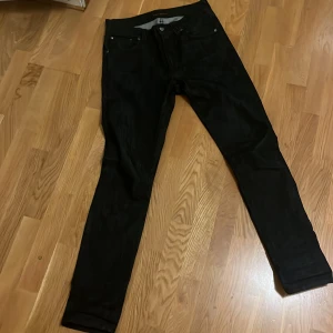 Svarta jeans från Nudie Jeans Co - Snygga svarta jeans från Nudie Jeans Co med en klassisk femficksdesign. De har en slim passform och är tillverkade i ett slitstarkt denimtyg. Perfekta för en stilren look, de är helt nya storlek w30/l32 hör gärna av er vid frågor.