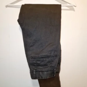 Grå kostymbyxor från Oscar Jacobson - Snygga grå kostymbyxor från Oscar Jacobson. Byxorna har en klassisk design med knappar och dragkedja framtill. Perfekta för en stilren look. Kostade närmare 2000 kr vid inköp.