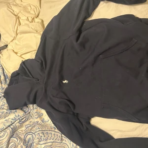  hoodie från Ralph Lauren - Säljer en stilren svart hoodie från Ralph Lauren med en liten vit logga på bröstet. Tröjan har en klassisk känguruficka och en bekväm huva. Perfekt för en avslappnad look.