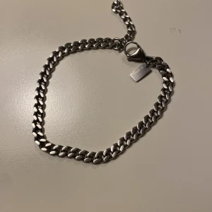 Silverfärgat armband - Stilrent silverfärgat armband med klassisk kedjedesign. Perfekt för att ge en elegant touch till din stil. Armbandet har en praktisk låsmekanism och en liten bricka som detalj.