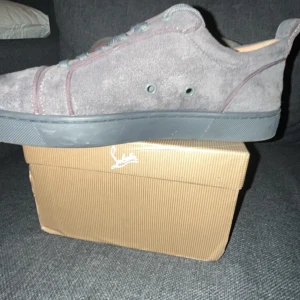 Grå sneakers från Christian Louboutin - Snygga grå sneakers i mocka från Christian Louboutin med den ikoniska röda sulan. Skorna har snörning och en stilren design som passar perfekt för en trendig look. Levereras med originalförpackning och äkthetsintyg.