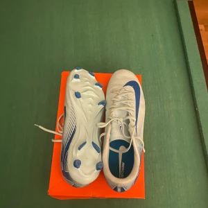 Vita och blå fotbollsskor från Nike - Snygga vit och blå fotbollsskor från Nike använda 1 gång inga defekter för utom lite grönt på sulan. finns uppe på main kontot @Veloce Fashion pm för frågor 