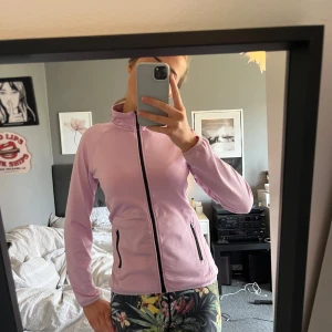 Rosa träningsjacka - Säljer en rosa träningsjacka med dragkedja framtill och fickor med dragkedjor. Jackan har en hög krage och långa ärmar, perfekt för träning.