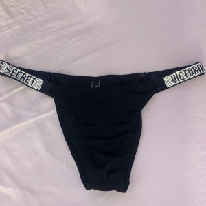 Svarta trosor från Victoria's Secret - Snygg svarta trosor från Victoria's Secret med glittriga detaljer på banden. Perfekt för en stilren och glamorös look. Bekväm passform med elastiska band.