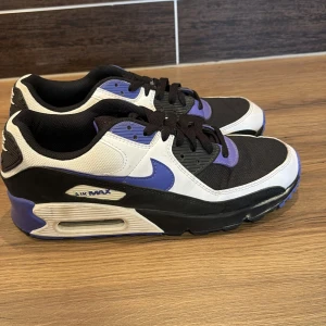 Nike Air Max - Snygga Nike Air Max sneakers i en cool färgkombination av svart, vit och lila. Skorna har en klassisk design med synlig Air Max-dämpning och snörning. Perfekta för en sportig look.