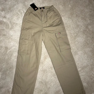 Dickies - Snygga beige cargobyxor från Dickies med praktiska fickor på sidorna. Byxorna har en dragkedja och knapp framtill samt elastisk midja för extra komfort. Perfekta för en avslappnad stil.